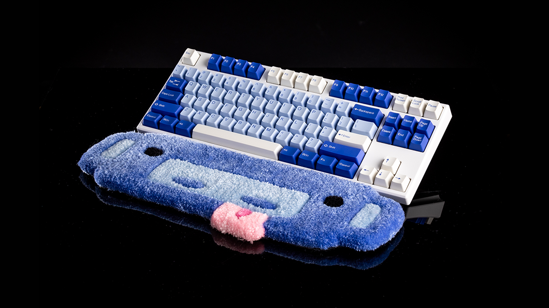 A keyboard rug shaped like Wumpus's head with their tongue sticking out, in front of a keyboard.